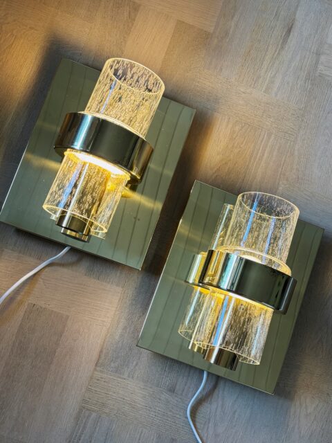To stilige vintage vegglamper i messing og klart luseglass fra Høvik Lys, designet av Jonas Hidle. Modell 7360, 1970-80-talls. Moderne stikk. Blank og fin messing, kun ørsmå bruksspor. Et lite avslag bak ved festet nederst på ene glasskuppelen, ikke synlig når lampen henger på veggen. Mål: H 28,5 cm. B 23,5 cm. Pris per stk: 1250 kr. Kjøpe nå med Vipps? Send melding. Må hentes, sendes ikke.