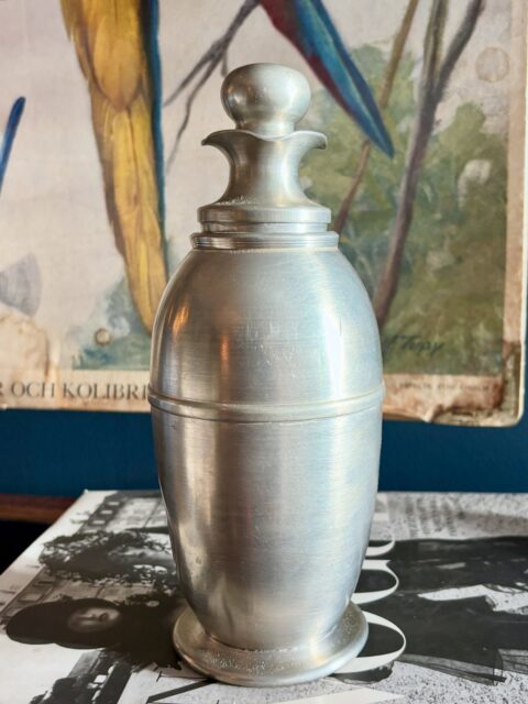 Superkul vintage/semiantikk art deco cocktailshaker i tinn fra I-K Tinn, Oslo, fra perioden 1930-50-tall. Med sil og toppkork (med kork). H 22 cm. Pen og i god vintagestand, tinn er dog et mykt metall, og shakeren har en liten bulk på ene siden. Ikke funksjonstestet. Pris: 450 kr. Kjøpe nå med Vipps? Send melding. Må hentes.🍸